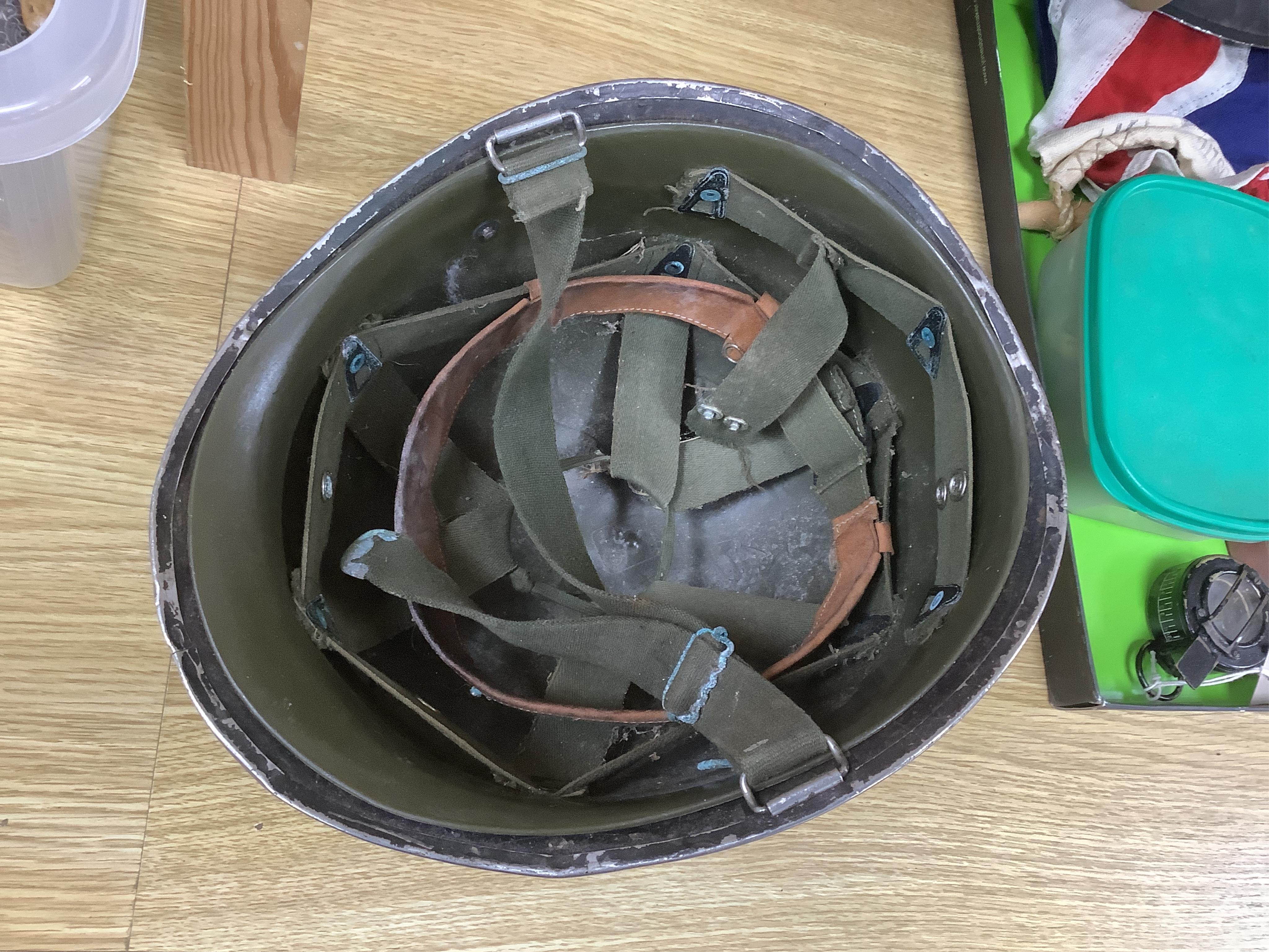 A collection of military items, including a U.S. Army helmet, an M42 helmet, a WWII British Home Front helmet, a Union flag 96cm x 60cm, a compass, a Kukri display shield, and a box of military cap badges, buttons, etc.